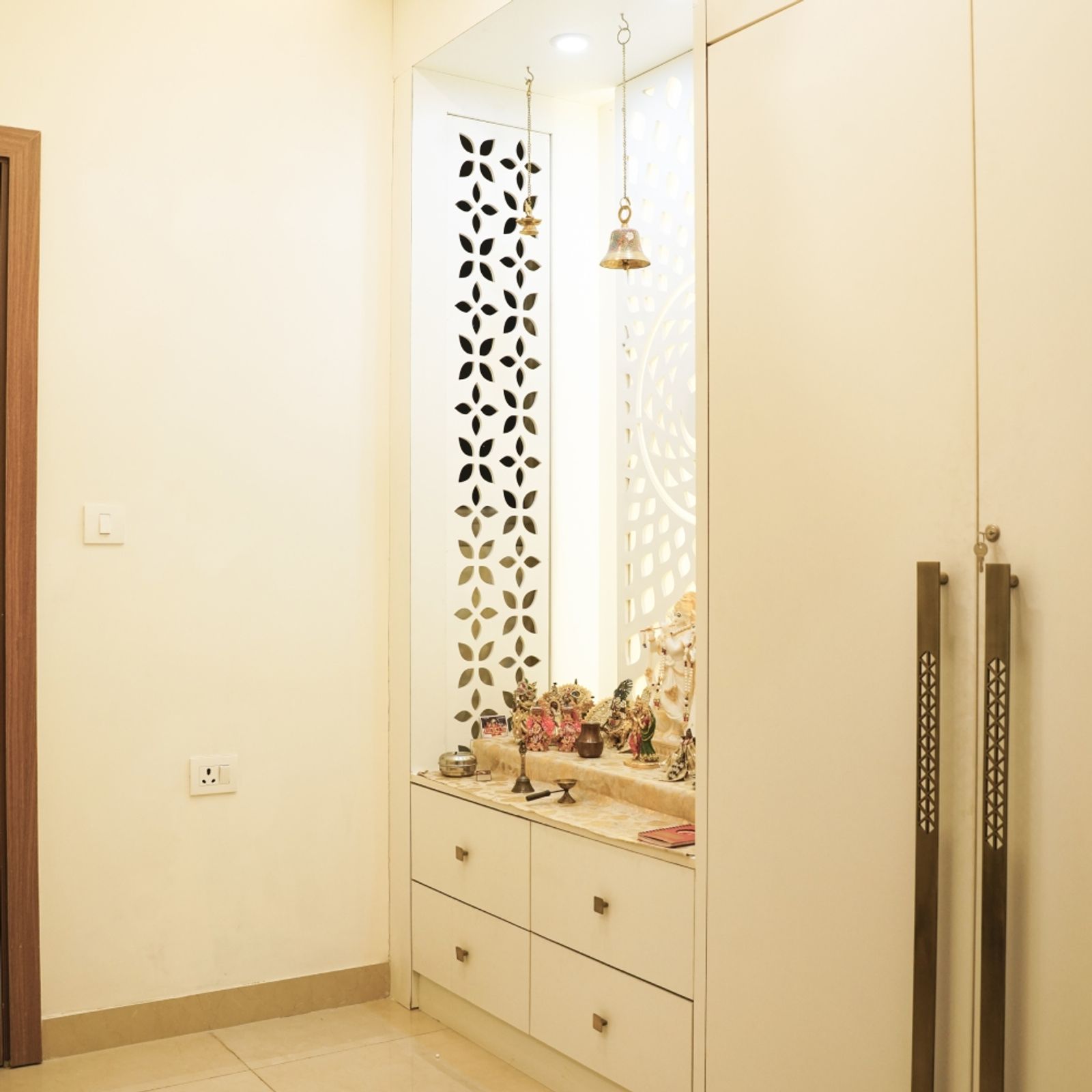 White Pooja Unit Design with CNC Cut Panels, Hanging Bells, and Drawer Storage
