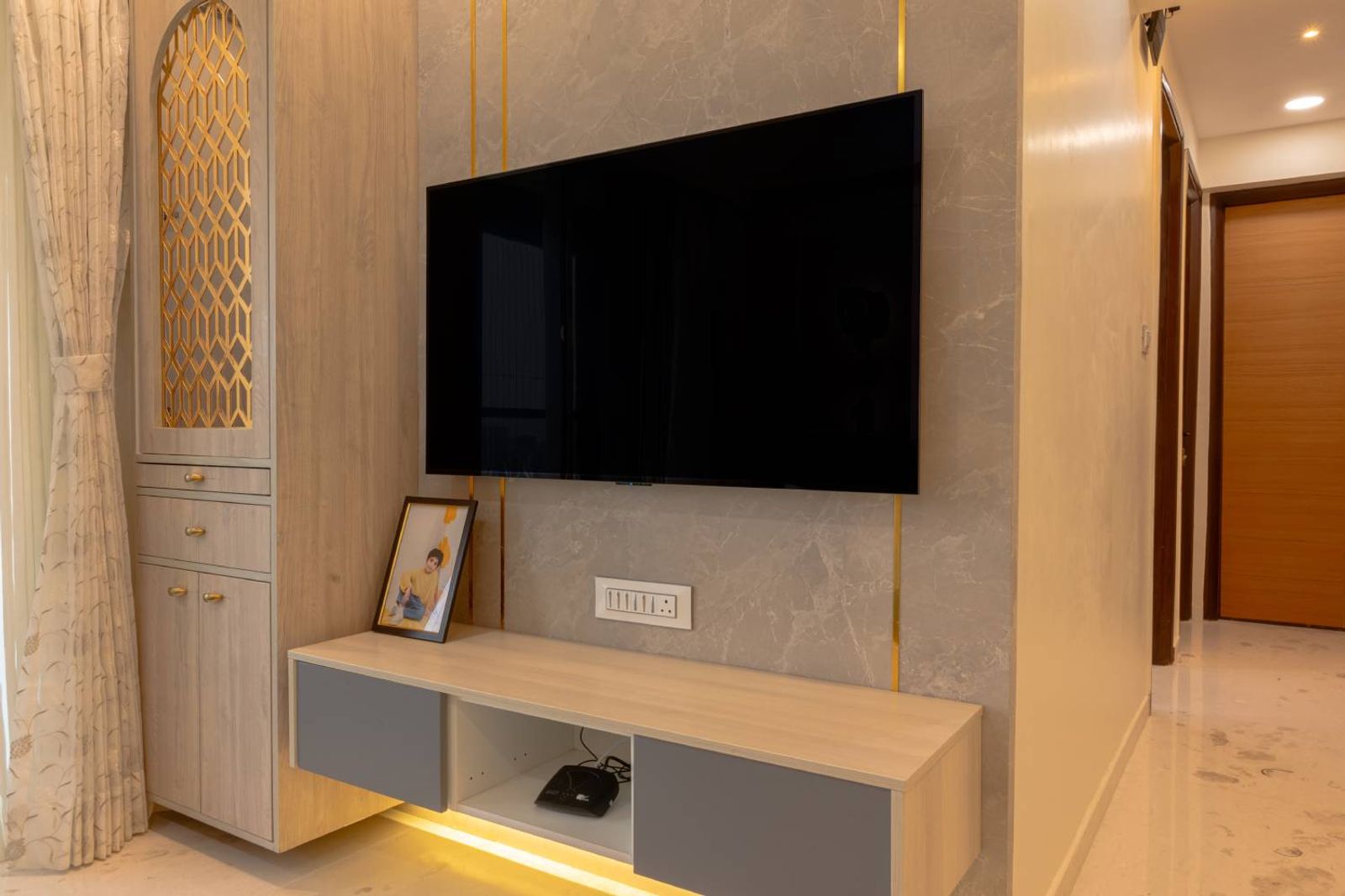 TV Unit with Grey Marble Patterned Wall with Gold Trims and Closed Door Pooja Unit
